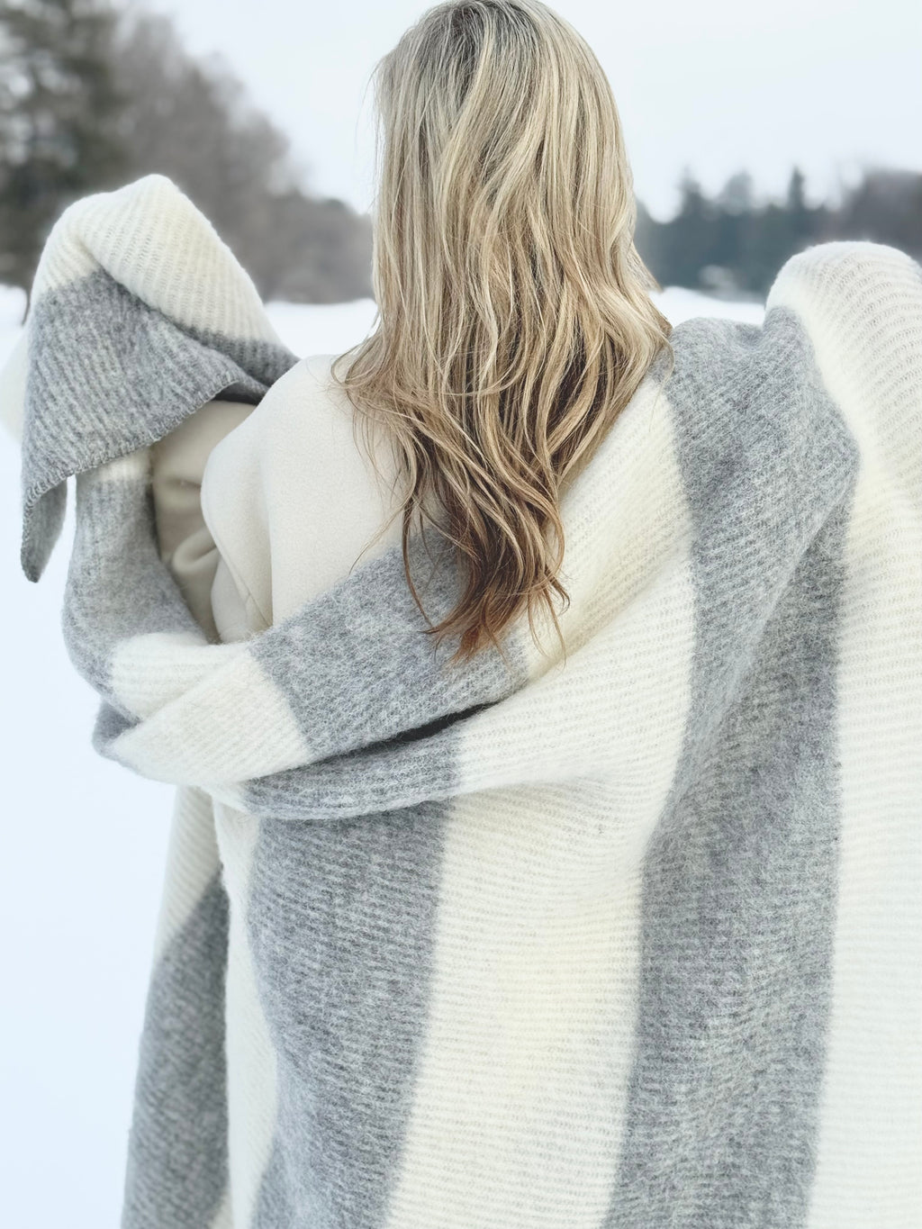 Person wrapped in a large gray and white blanket in a snowy landscape